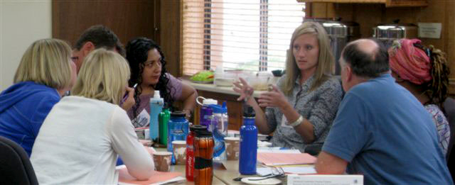 A group of people around a table, one woman talking.