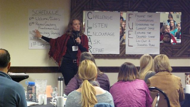 Woman standing by whiteboard, she is facing a group of people.